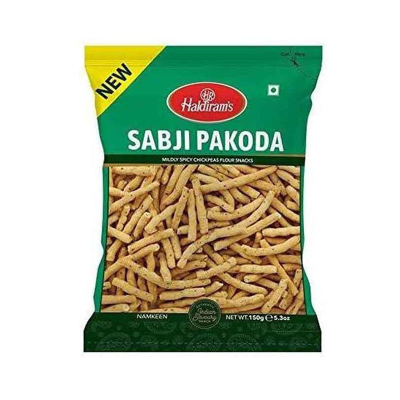 A package of Haldiram's Sabji Pakoda, showing the crispy fried snack through a transparent window. The packaging is predominantly green with product name and weight (150g) visible.