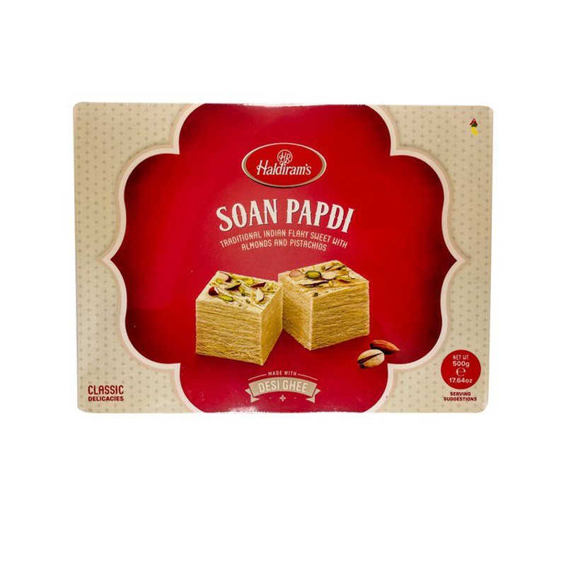 Packaging of Haldiram's Soan Papdi 500g with the product visible through a red circular window. The background is white with a decorative pattern and the brand logo is at the top.
